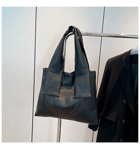Detail of black faux leather tote bag with circular orange embroidery and soft texture