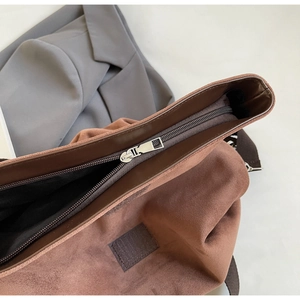 Detail shot of brown suede tote bag featuring silver metal zipper and dark leather trim