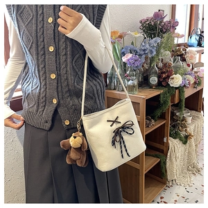 Detail of white canvas bucket bag with brown bow and cute plush puppy charm