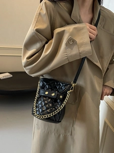 Quilted black bucket bag with gold chain strap worn with a stylish khaki trench coat