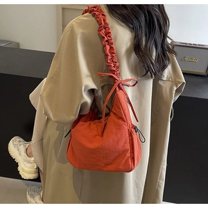 Detail van oranje hobo tas met geplooide schouderband en trekkoord aan de zijkant