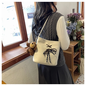 Off-white suede bucket bag with black bow detail and bear charm worn by a model