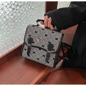 Detailed view of houndspur pattern, metallic bow buckle, and faux leather trim on backpack
