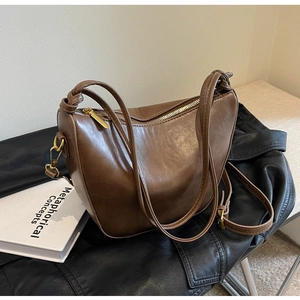 Close-up of brown crescent hobo bag in glossy PU leather with elegant gold hardware