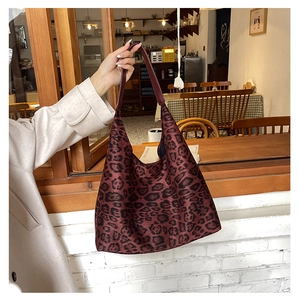 Close-up of leopard print tote bag with red leather handle in a cozy cafe setting