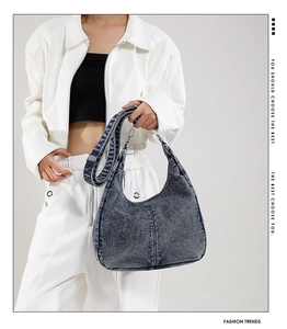 Detail of blue denim crescent bag featuring adjustable strap and silver metal hardware