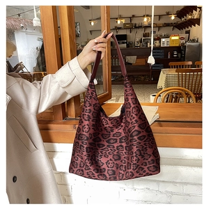 Detail of burgundy leopard print tote bag held by a person in a cozy cafe setting