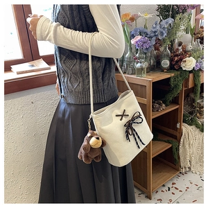 Detail view of cream canvas bucket bag with bow tie and cute puppy plush pendant charm