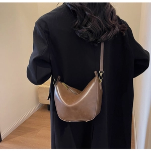 Rear view of a brown leather crescent hobo bag worn crossbody with golden hardware accents