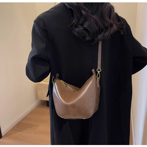 Detail view of a vintage brown leather crescent bag with gold zipper and thin strap