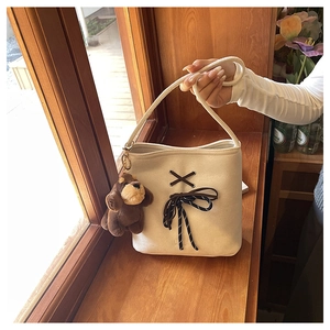 Detail of canvas bucket bag with woven rope handle and plush puppy pendant on a wooden ledge