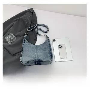 Blue denim half-moon shoulder bag shown with tablet and phone for size comparison
