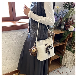Detail of white canvas crossbody bag with navy bow and cute brown puppy plush pendant