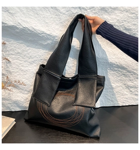 Close-up of large black leather tote bag featuring orange circular embroidery detail