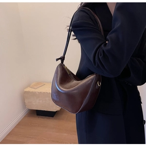 Detail of a dark brown crescent shoulder bag with golden zipper and knot strap detail