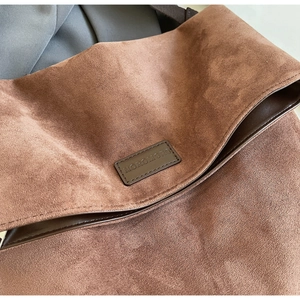 Detail of brown suede tote bag featuring leather logo patch and textured fabric finish