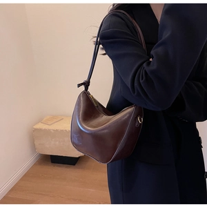 Fashionable dark brown leather hobo bag worn by a model in a black blazer suit