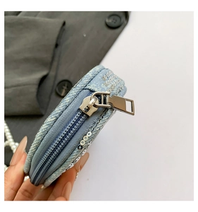 Détail d'un petit porte-monnaie rond en denim bleu avec paillettes argentées et zip métal