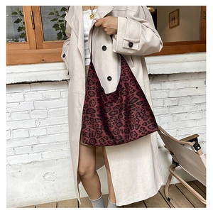 Detail view of large leopard print tote bag in burgundy canvas worn with beige coat