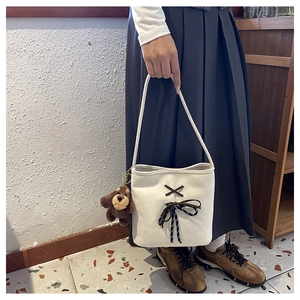 Detail of white canvas bucket bag featuring a brown decorative bow and plush dog charm