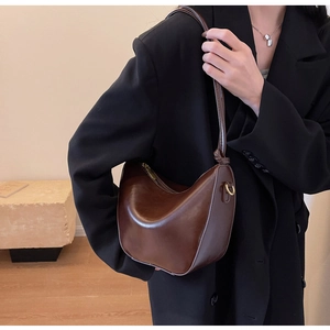 Detail of a dark brown half-moon leather shoulder bag with smooth texture and golden D-ring