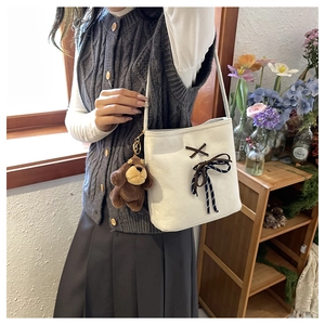 Close-up of white canvas bucket bag with brown bow decoration and plush bear charm