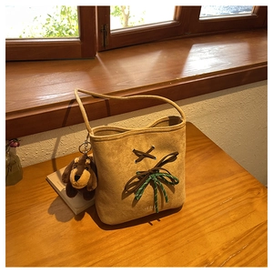 Brown suede bucket bag detail with leather lace-up, woven bow, and cute puppy charm