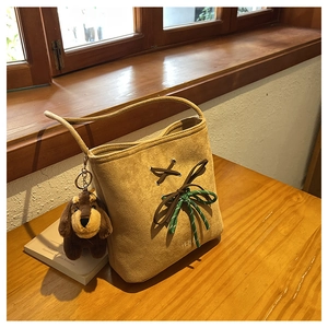 Detail of suede bucket bag featuring cross-laced straps and a cute plush dog charm
