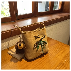 Detail view of khaki suede bucket bag with braided knot and cute puppy plush charm