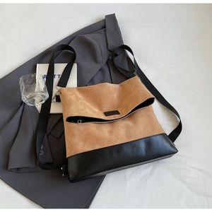 Detail of a large brown suede and black leather tote bag on a grey suit jacket
