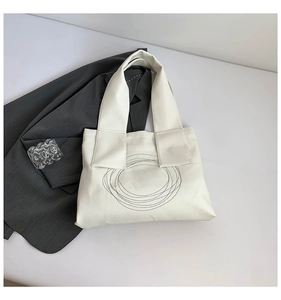 Close-up of white leather tote bag with abstract black circular embroidery and shoulder strap
