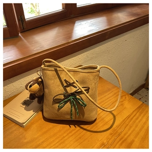 Detail of suede bucket bag with decorative rope bow and brown dachshund plush charm