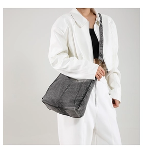 Detailed view of gray washed denim crossbody bag worn by a model in casual outfit