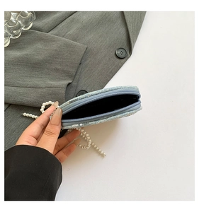 Détail du mini sac en denim bleu montrant la doublure noire et la chaîne perlée