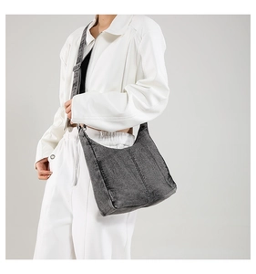 Detail of grey washed denim hobo bag featuring vertical stitching and adjustable strap