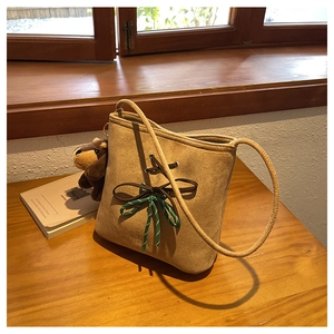 Detail of suede bucket bag featuring leather bow and green cord on wooden surface