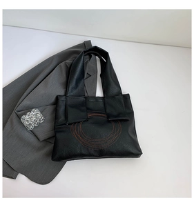 Detail of black tote bag featuring brown concentric circle stitching and wide handle