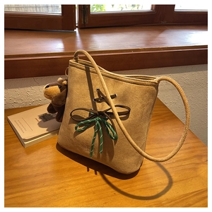 Close-up of camel suede bucket bag with woven rope bow knot and plush bear charm