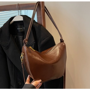 Detail of a dark brown glossy leather crescent bag with golden hardware and zipper