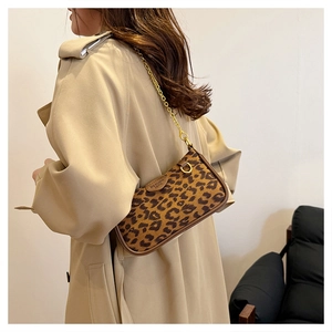 Detail of leopard print underarm bag with gold chain strap worn by a model in a trench coat