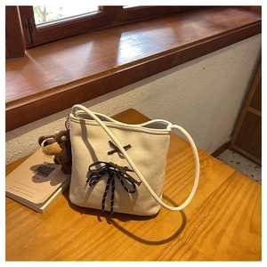Detail of cream suede bucket bag featuring brown bow accent and plush puppy charm