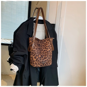 Detail of leopard print bucket bag with leather handles shown against a dark suit