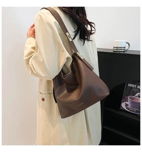 Detailed view of dark brown soft leather hobo bag with gold logo on beige trench coat