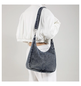 Detail of vintage washed blue denim hobo bag with wide shoulder strap and silver metal clip