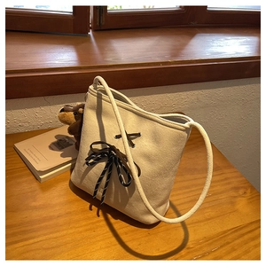 Detail of a creamy white suede bucket bag featuring a dark brown ribbon bow decoration