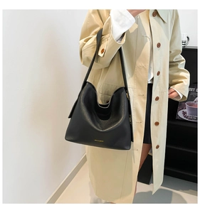 Detail of minimalist black leather tote bag with subtle gold logo on a beige trench coat