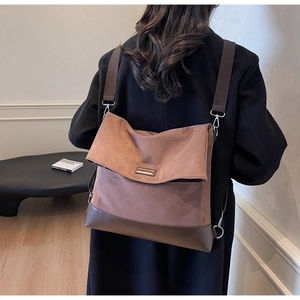 Detail view of large brown canvas tote bag with leather bottom and metal nameplate