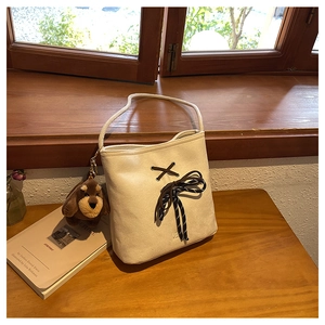 Detail of cream suede bucket bag with contrast brown rope bow and plush dog charm