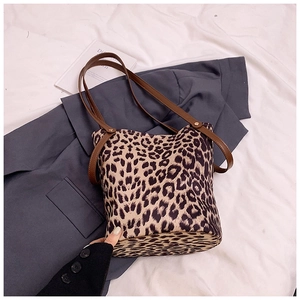 Chic leopard print bucket tote bag with leather straps on a gray blazer backdrop