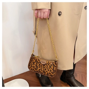 Detail of leopard print shoulder bag with gold chain strap held by a model
